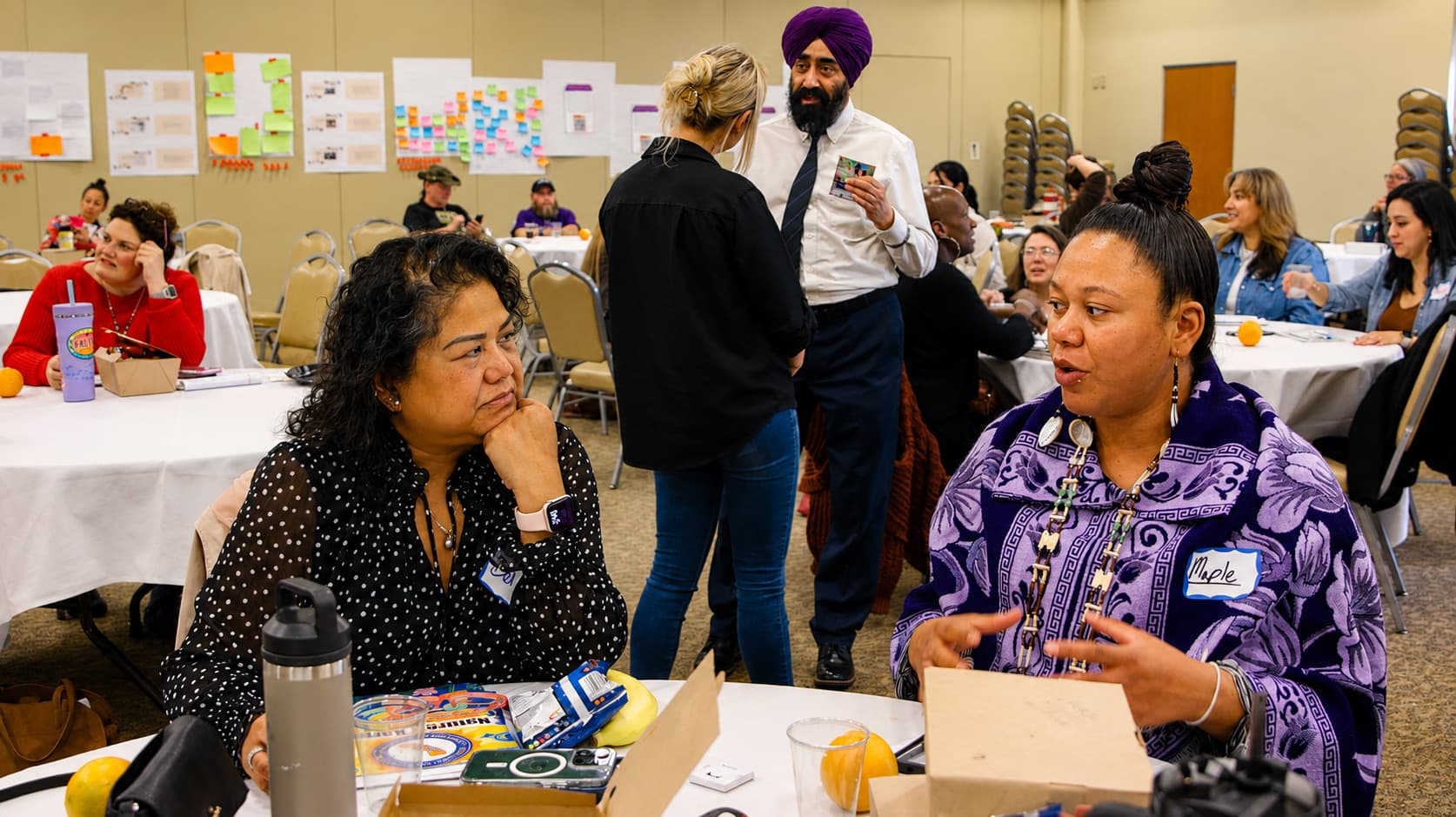 Community members in conversation at round tables during a Butte Resilience Collaborative convening, with workshop notes and sticky notes covering the wall behind them.