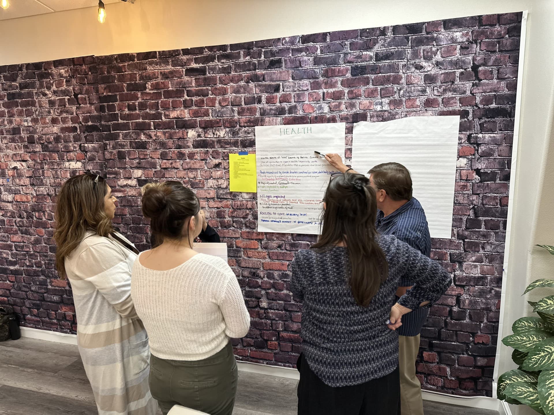 Four Butte Resilience Collaborative participants standing at a wall, reviewing a hand-written flip chart headed "Health" during a planning session.